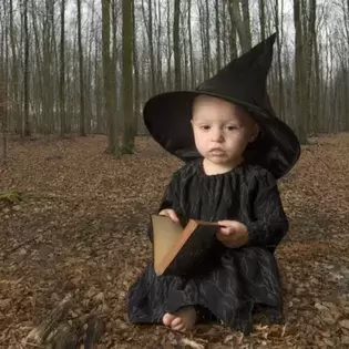 small child dressed as a witch holding a grimoire standing in spooky woods