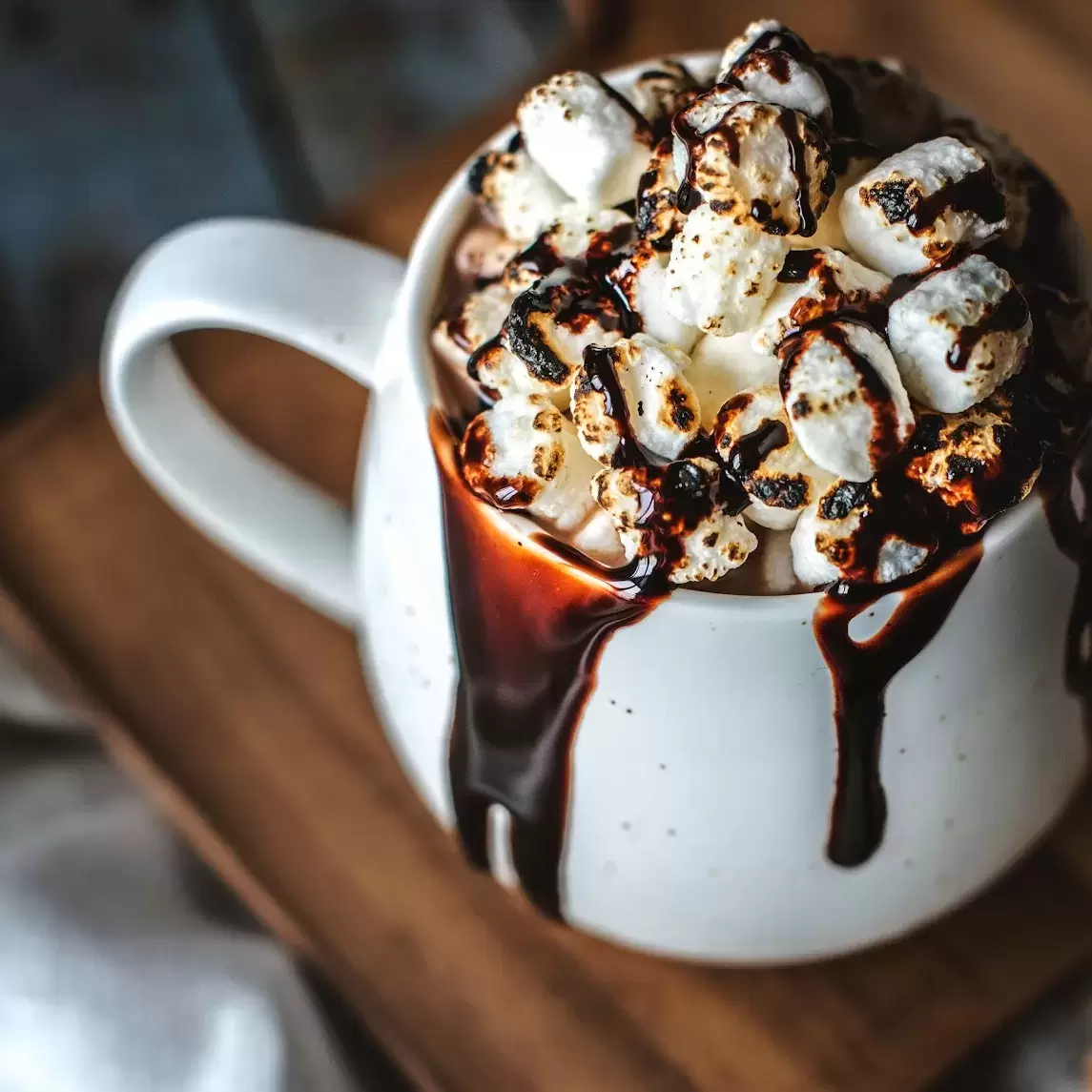 mug of overflowing hot chocolate with loads of marshmallows drizzled in chocolate