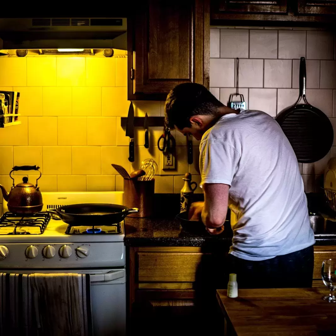 someone with their back to the camera as they prepare some type of meal in their dimly-lit kitchen