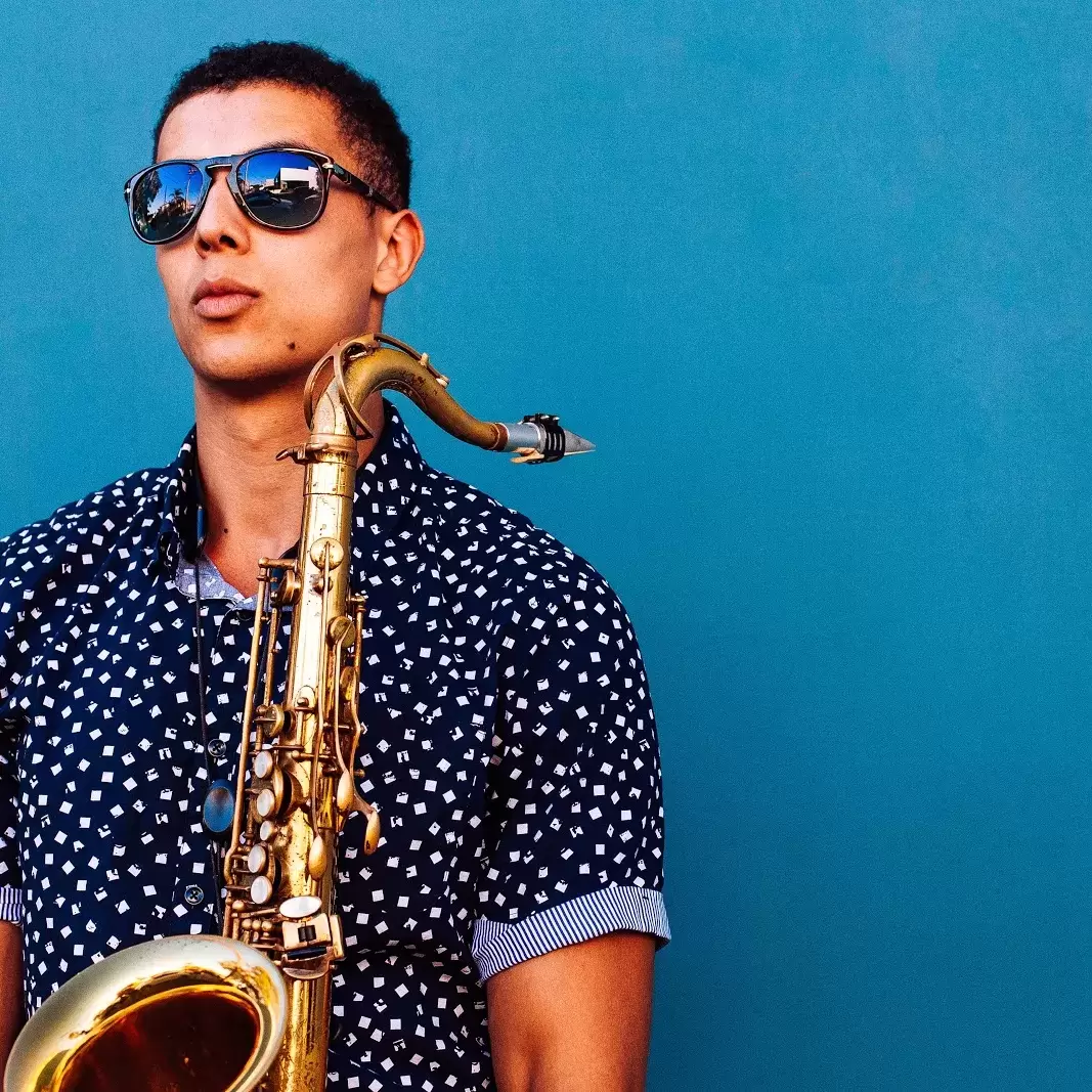 a person with short hair holding a saxophone and wearing a pair of dark sunglasses