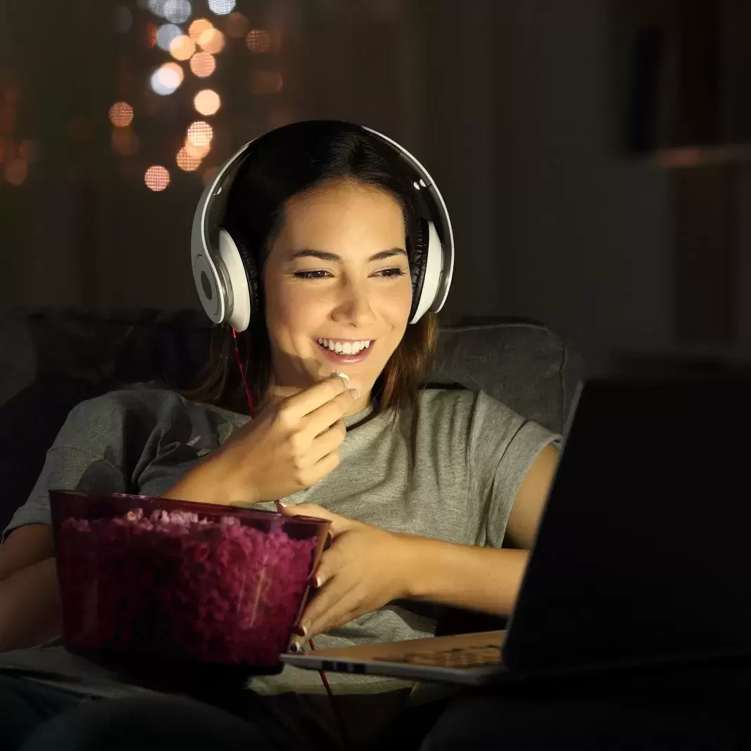 Person looking at a laptop screen with headphones on while eating popcorn