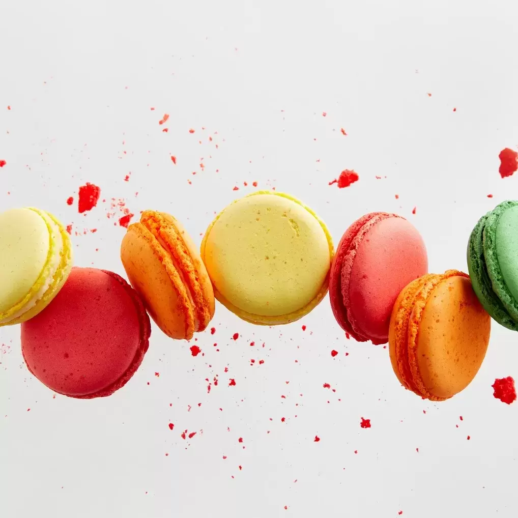 a display of colorful macarons splashed across a pale background