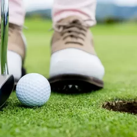 cut off shot of a person in golfing shoes attempting a putt. 