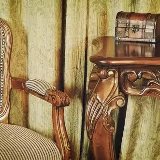 antique chair next to an ornate table with a small vintage chest on top of it. 