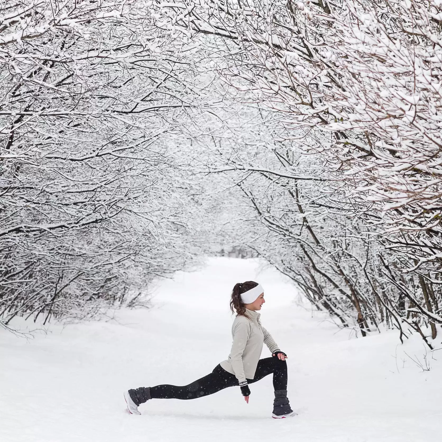 A woman stretching between snowy trees.